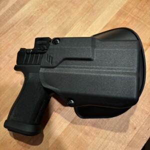 Black handgun holstered in a black polymer holster on wooden surface.